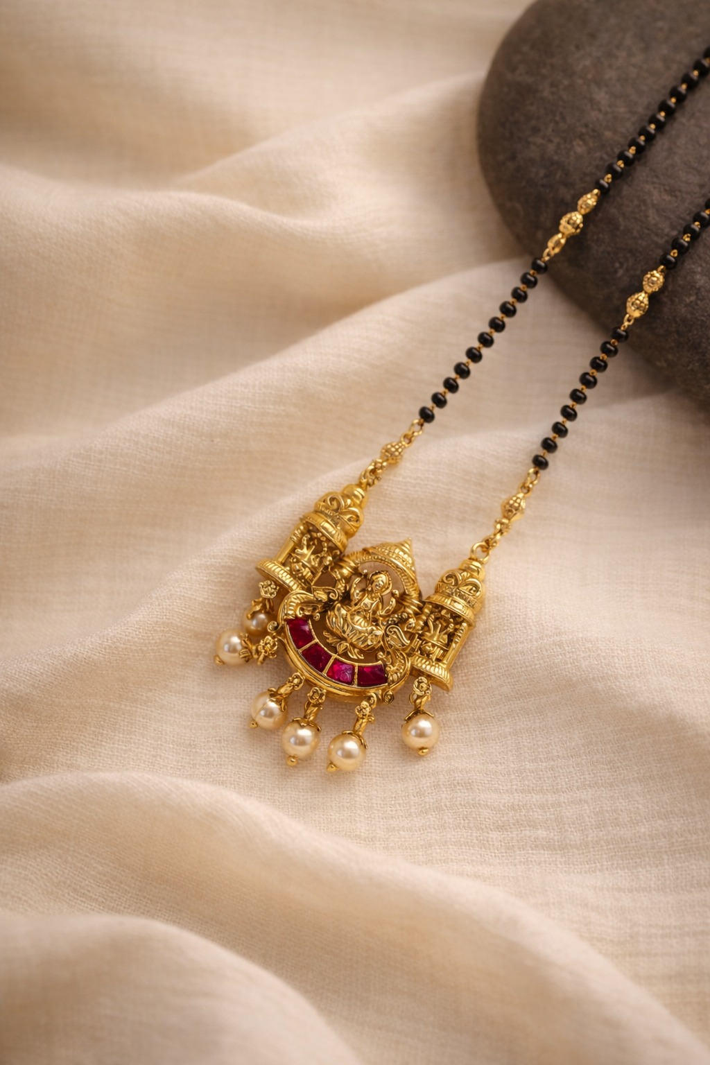 Gold necklace with red stone and pearl pendants on a beige fabric background
