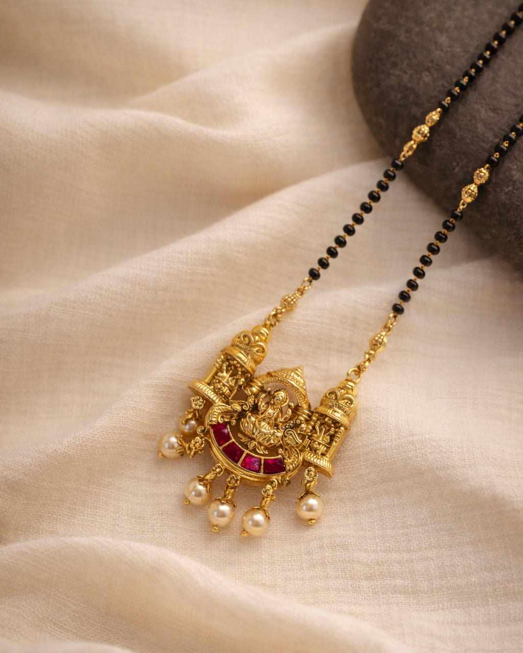 Gold necklace with red stone and pearl pendants on a beige fabric background