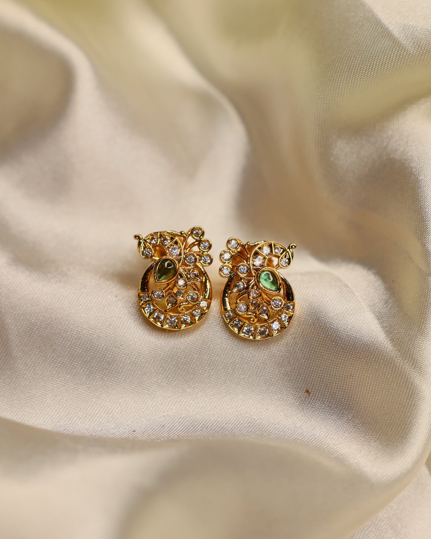Gold pineapple-shaped earrings with green centers on a beige fabric background