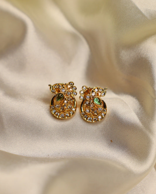 Gold pineapple-shaped earrings with green centers on a beige fabric background