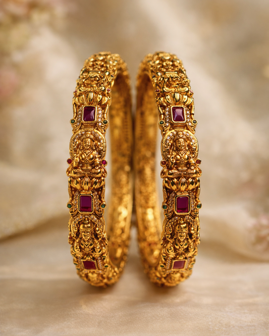 Pair of gold bangles with red gemstones on a soft, blurred  suwarnikaa jewels background