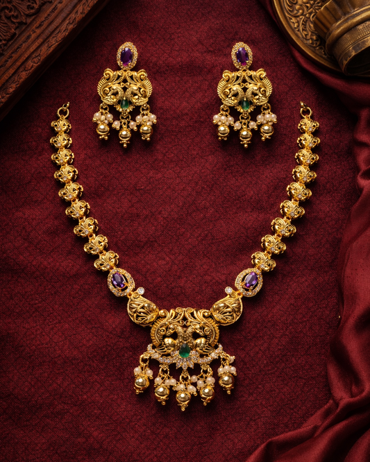 Gold necklace with green and purple stones on a red fabric background suwarnikaa jewels www.suwarnikaajewels.com 